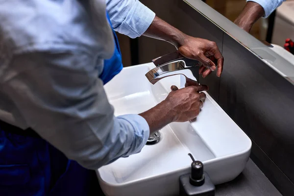 Primer plano de plomeros negros irreconocibles tratando de abrir un grifo de agua en el baño — Foto de Stock