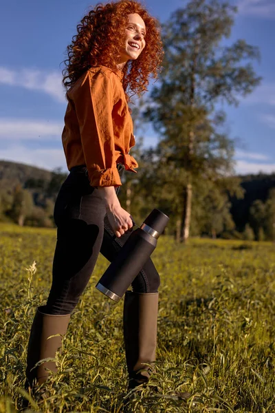 Fiatal vörös hajú nő alkalmi viselet termoszban a kezében a területen, séta — Stock Fotó