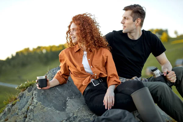 美しい白人のカップルは休憩を取って座って、山の上で休み、お茶を飲む — ストック写真