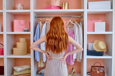 Evdeki kadın, askı rafının önünde dikiz aynasıyla kıyafet seçmeye çalışıyor.