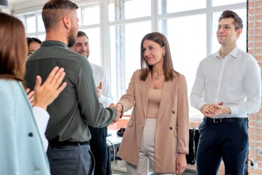 İş arkadaşları birbirlerini selamlıyor, modern ofiste el sıkışıyorlar.