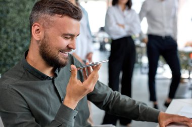 Genç beyaz adam cep telefonunu elinde tutuyor, konuşuyor ve sesli mesajları dinliyor.