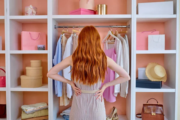 Evdeki kadın, askı rafının önünde dikiz aynasıyla kıyafet seçmeye çalışıyor.