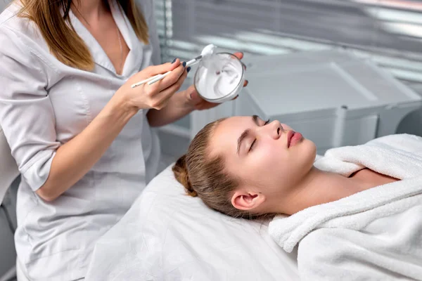 Cosmetologo ritagliato applicando maschera da ciotola su bella faccia di donna, in spa — Foto Stock