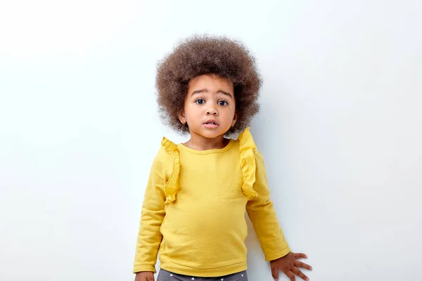 Schattig kind meisje met pluizig krullend haar kijken naar camera met verrast gezichtsuitdrukking — Stockfoto