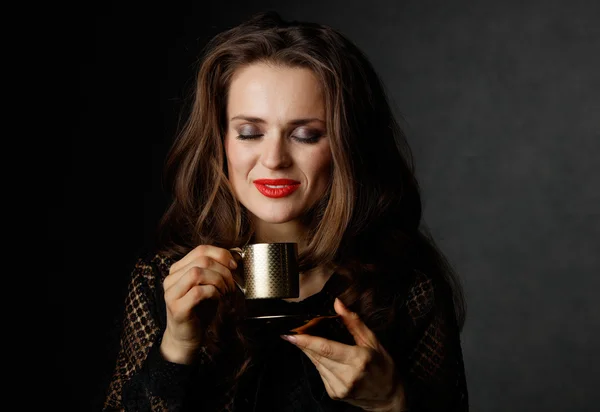 Mulher com lábios vermelhos apreciando xícara de café no fundo escuro — Fotografia de Stock