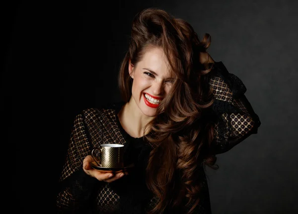 Mujer alegre sosteniendo taza de café sobre fondo oscuro — Foto de Stock