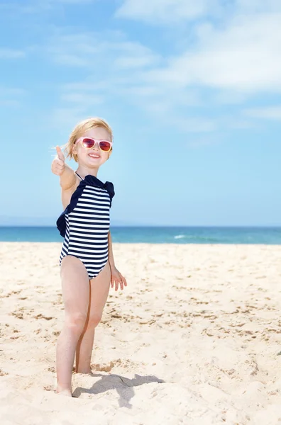 Happy girl in swimsuit on a white beach showing thumbs up — Stock Photo, Image