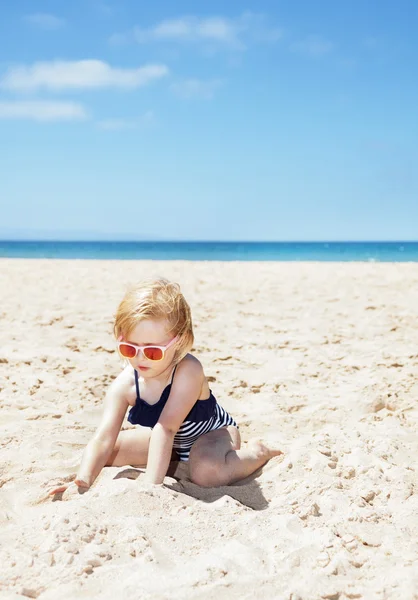 Happy girl in striped swimsuit playing with sand on white beach — Stock Photo, Image