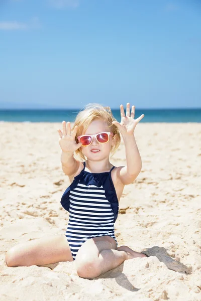 Girl in striped swimsuit on a white beach showing sandy hands — Stock Photo, Image