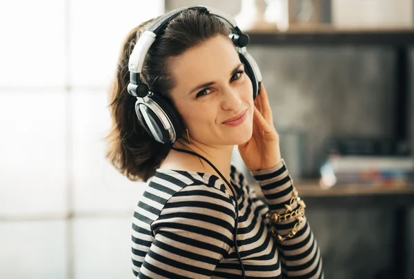 Nainen kuuntelee musiikkia kuulokkeiden kautta parvella asunnossa — kuvapankkivalokuva