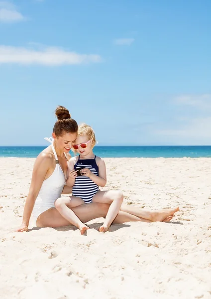 Glad mor og barn på stranden kigger på fotos i kameraet - Stock-foto