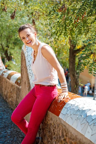 グエル公園で trencadis スタイルのフェンスの上に座って笑顔の女性 — ストック写真