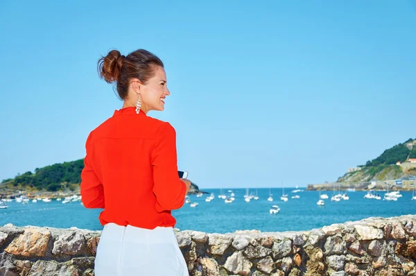 Sett bakifrån kvinna med mobil stående framför lagunen — Stockfoto