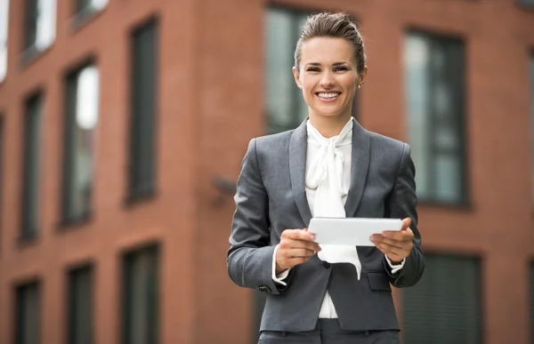 Femme d'affaires souriante utilisant une tablette PC contre un immeuble de bureaux — Photo