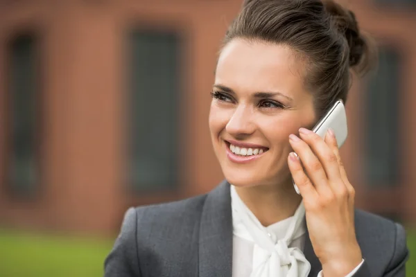 Улыбающаяся деловая женщина возле офисного здания разговаривает со смартфоном — стоковое фото