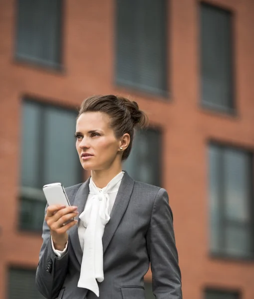 Mujer de negocios moderna contra edificio de oficinas con teléfono inteligente —  Fotos de Stock