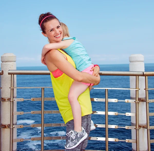 Smiling mother and child in fitness outfit hugging on embankment — Stock Photo, Image