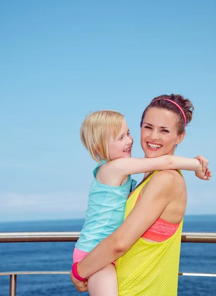 Happy mother and child in fitness outfit hugging on embankment — Stock Photo, Image