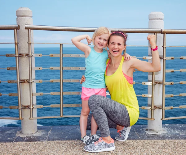 Matka a dítě v fitness oblečení na nábřeží ukazující biceps — Stock fotografie