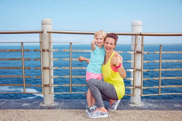 Feliz fitness madre e hijo en terraplén mostrando los pulgares hacia arriba — Foto de Stock