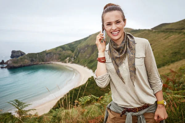 Woman hiker talking on mobile in front of ocean view landscape — Stockfoto