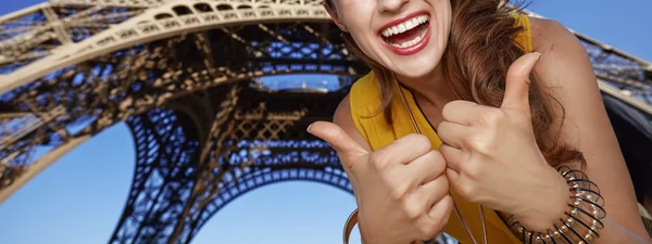 Улыбающаяся молодая женщина, показывающая большие пальцы перед Эйфелевой башней — стоковое фото