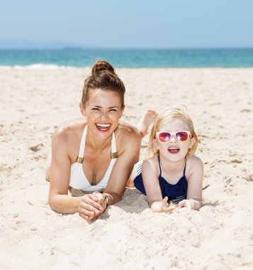Anne ve çocuk kumsalda döşeme mayolar içinde gülümseyen