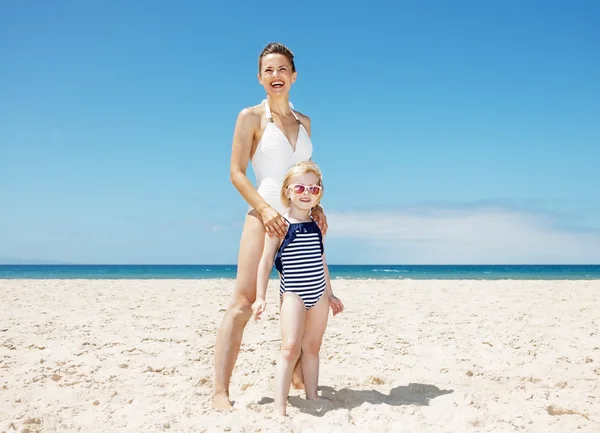 Feliz madre y niña en trajes de baño en la playa de arena en un día soleado — Foto de Stock