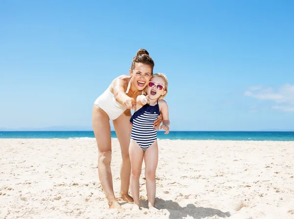 Sorridente madre e bambino che puntano in macchina fotografica sulla spiaggia sabbiosa — Foto Stock