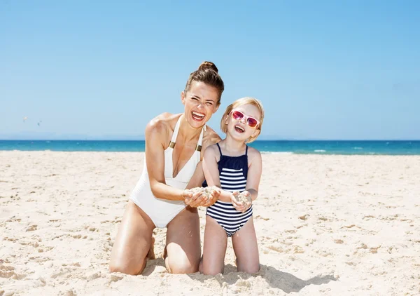 Gelukkig moeder en kind op strand met handen vol zand — Stockfoto