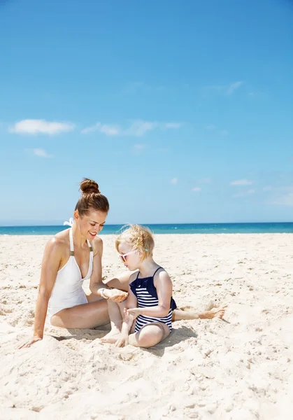 Smiling mother and girl in swimsuits at sandy beach playing — Stock Photo, Image