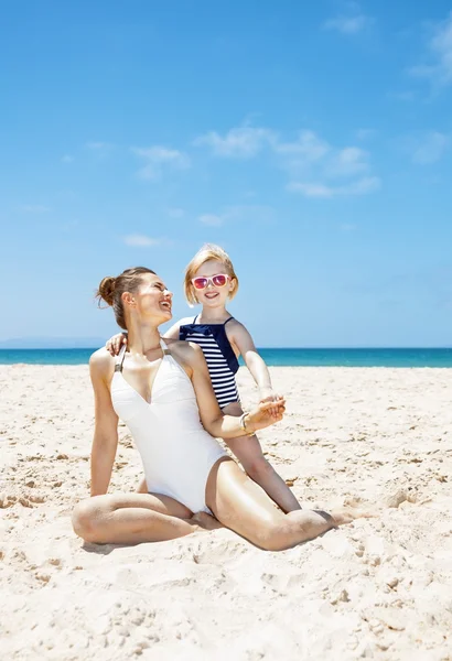 Gelukkig moeder en kind in zwemkleding aan zandstrand op zonnige dag — Stockfoto