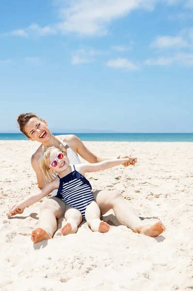 Mãe feliz e criança em maiôs na praia de areia jogando — Fotografia de Stock