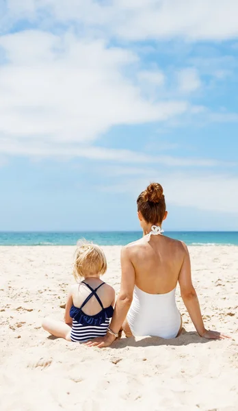 Visto da dietro madre e bambino in costume da bagno seduto in spiaggia — Foto Stock