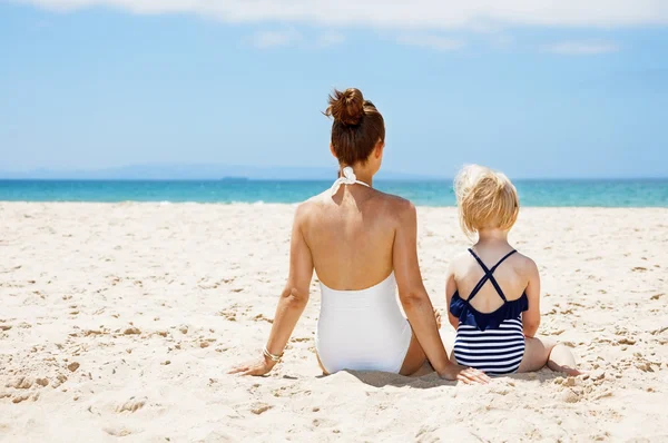 Seen from behind mother and child in swimsuits sitting at beach — Stock Photo, Image