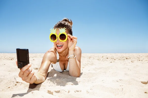 Mujer sonriente en gafas de piña tomando selfie en la playa de arena —  Fotos de Stock