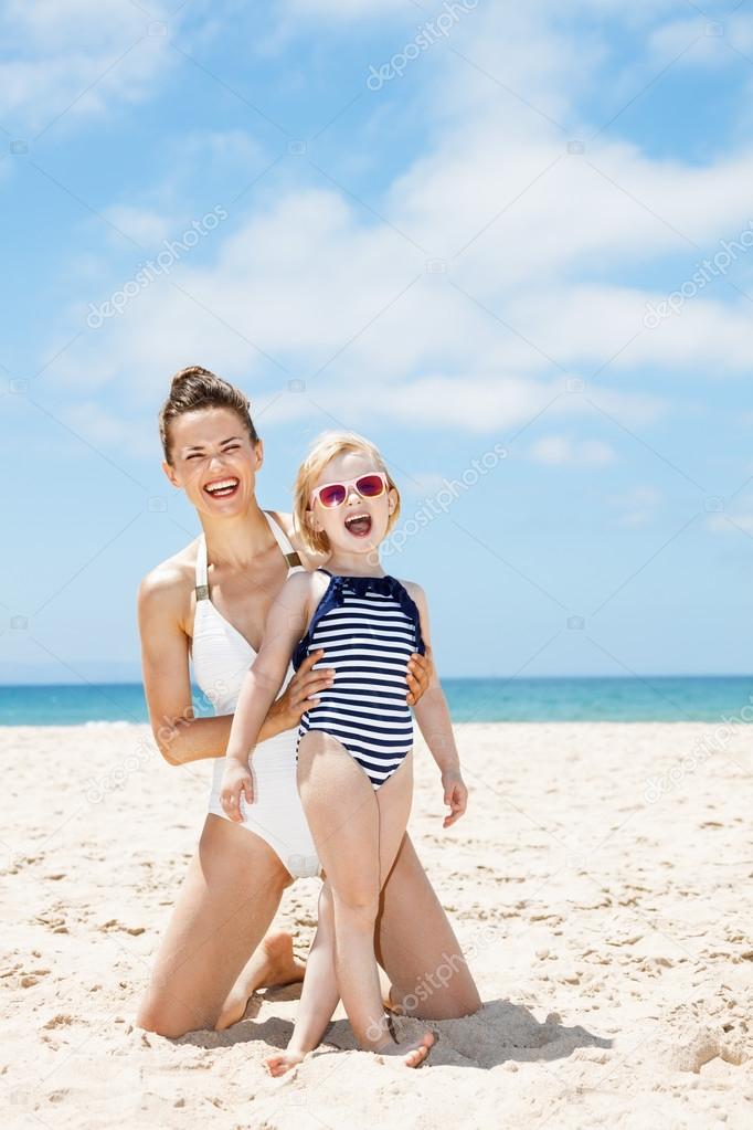 Smiling mother and child in swimsuits at beach on a sunny day