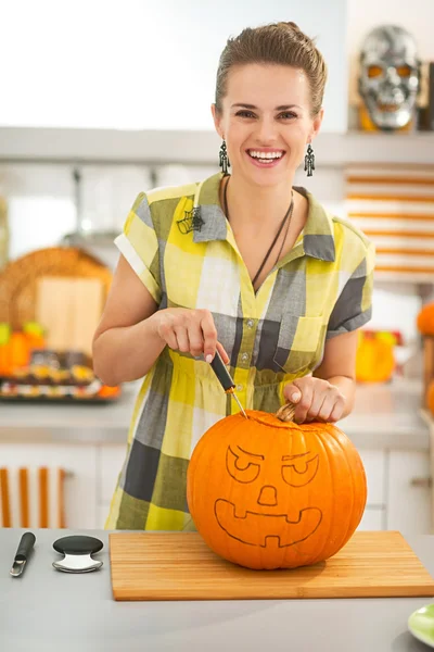 Woman in kitchen carving big orange pumpkin Jack-O-Lantern — Zdjęcie stockowe