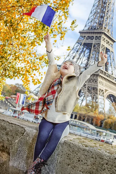 Child rejoicing and rising flag while sitting on parapet, Paris — Stockfoto