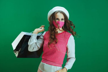 Covid-19 salgını sırasında hayat. Pembe tıbbi maskeli ve yeşil renkli alışveriş çantalı beyaz bereli genç bayan..