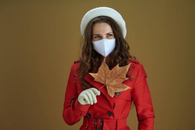 Covid-19 salgını sırasında hayat. Sarı sonbahar akçaağaç yaprağı ve bej arka planda kırmızı ceketli, modaya uygun orta yaşlı ev hanımı..