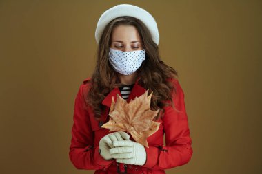 Koronavirüs salgını sırasında hayat. Kahverengi arka planda sarı sonbahar akçaağaç yaprağı olan kırmızı ceketli rüya gibi orta yaşlı kadın..