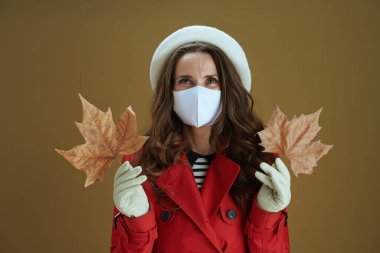 Merhaba sonbahar. 40 yaşında, kırmızı ceketli, kahverengi arka planda sarı sonbahar akçaağaç yaprağı olan moda bir ev hanımı..