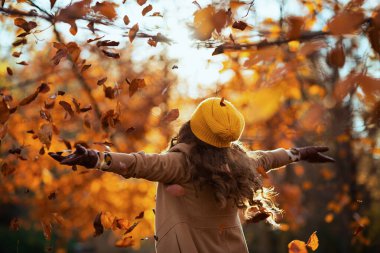 Merhaba Kasım ayı. Kahverengi ceketli, sarı şapkalı, gülen modern kadın sonbaharda şehir parkında neşe saçıyor..