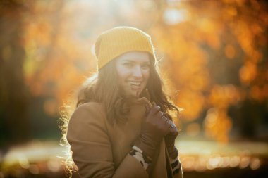 Merhaba Eylül. Mutlu, orta yaşlı, kahverengi paltolu ve sarı şapkalı bir kadın. Sonbaharda şehir parkında soğuk havada giyilen kıyafetlere sarılıyorlar..