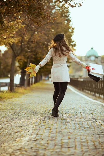 10月だ 幸せなトレンディーな40歳の女性でベージュトレンチコートと黒ベレー帽でショッピングバッグと秋に街の外の黄色の葉秋 — ストック写真