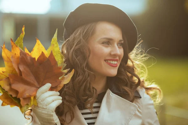 11月だ 幸せな現代40歳の女性でベージュトレンチコートと黒ベレー帽付き秋の黄色の葉屋外で市内秋 — ストック写真