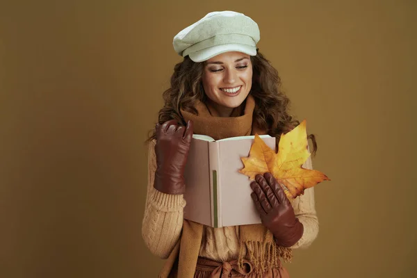10月だ スタイリッシュな中年主婦でセーターに黄色の秋のカエデの葉 本と革の手袋ブロンズ背景に隔離 — ストック写真