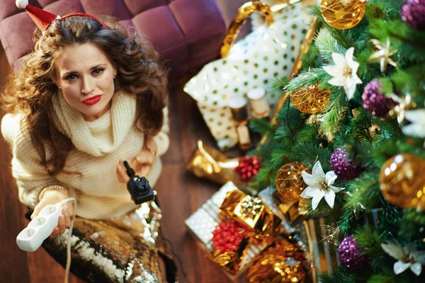 圣诞快乐 身着金色紧身衣裙和毛衣 头戴电源插座的40岁时髦女士在圣诞树旁和礼品盒的上图 — 图库照片